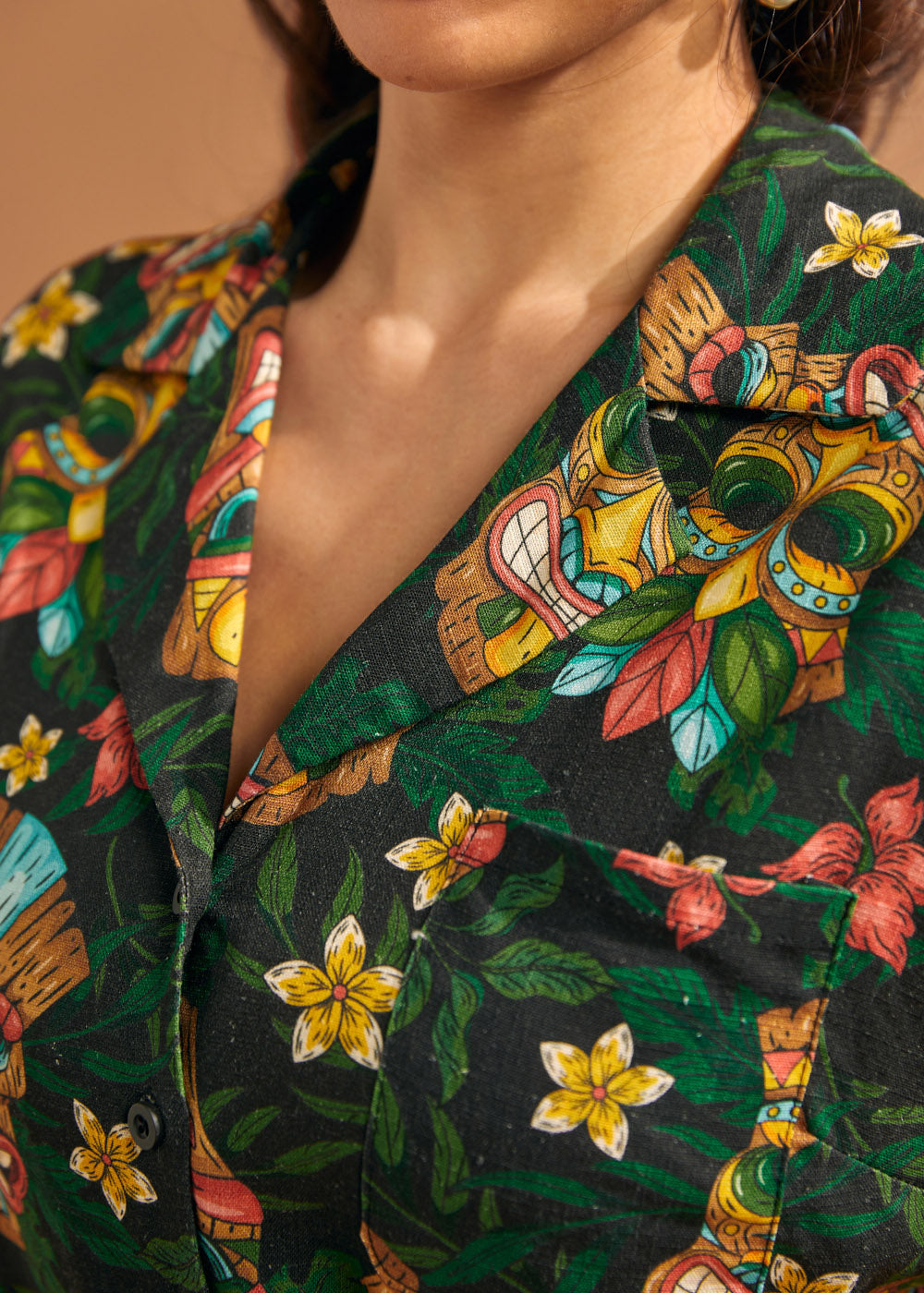 Close-up of camp collar and colorful tiki mask print on tropical blouse.