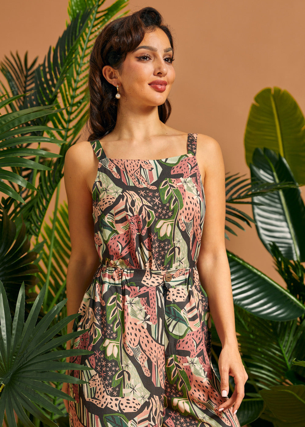 Woman wearing a floral tank top standing among tropical plants with a brown background