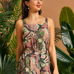 Woman wearing a floral tank top standing among tropical plants with a brown background