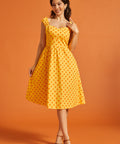 Woman wearing a yellow polka dot cotton fit and flare midi dress with sweetheart neckline and pockets.