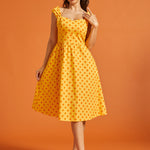 Woman wearing a yellow polka dot cotton fit and flare midi dress with sweetheart neckline and pockets.