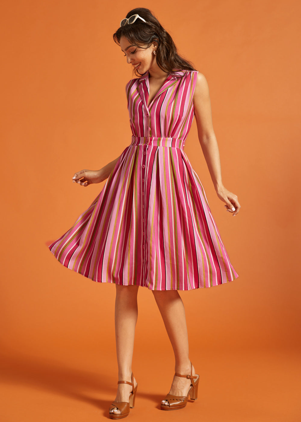 Woman wearing a pink striped sleeveless button-front midi dress with side pockets.