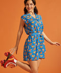 Woman wearing a blue roller skate print romper with a tie waist and cap sleeves.