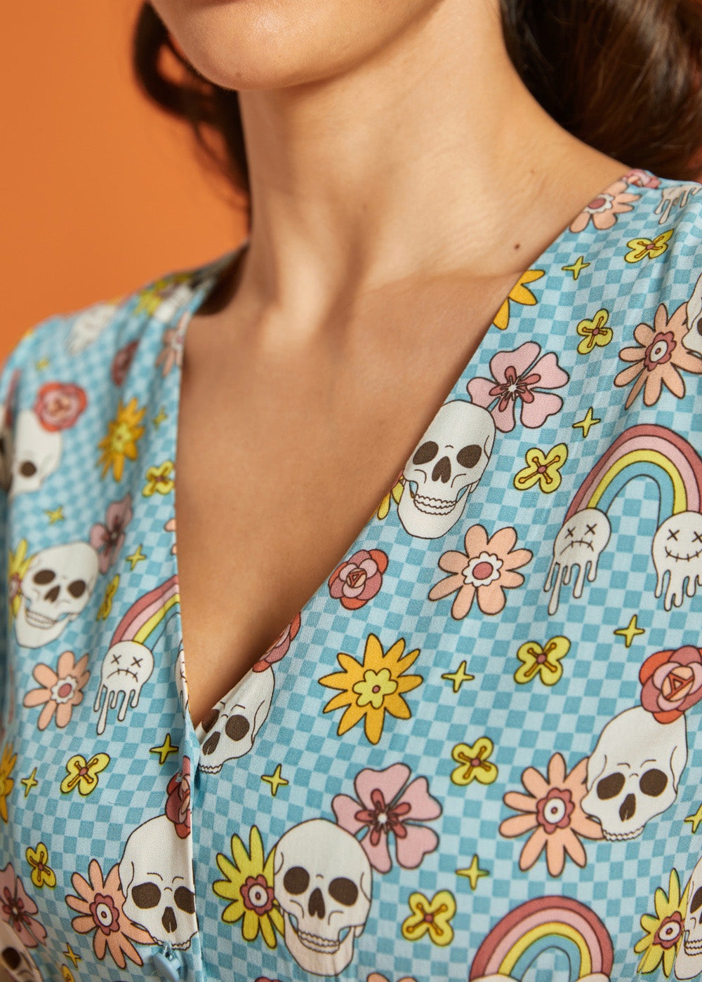 Close-up of V-neckline featuring checkerboard novelty print with skulls, flowers and melting rainbows.