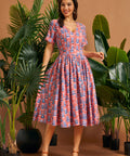 Woman wearing a coral vintage-inspired tiki print fit and flare midi dress with pockets.