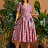 Woman wearing a coral vintage-inspired tiki print fit and flare midi dress with pockets.
