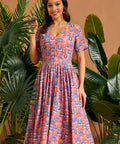 Woman wearing coral tiki print fit and flare dress with side pockets.
