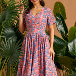 Woman wearing coral tiki print fit and flare dress with side pockets.