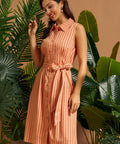 Woman wearing a peach pinstriped midi shirt dress with a waist tie.