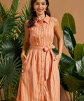Woman wearing a peach striped sleeveless linen blend shirt dress with a self-tie waist.