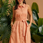 Woman wearing a peach striped sleeveless linen blend shirt dress with a self-tie waist.
