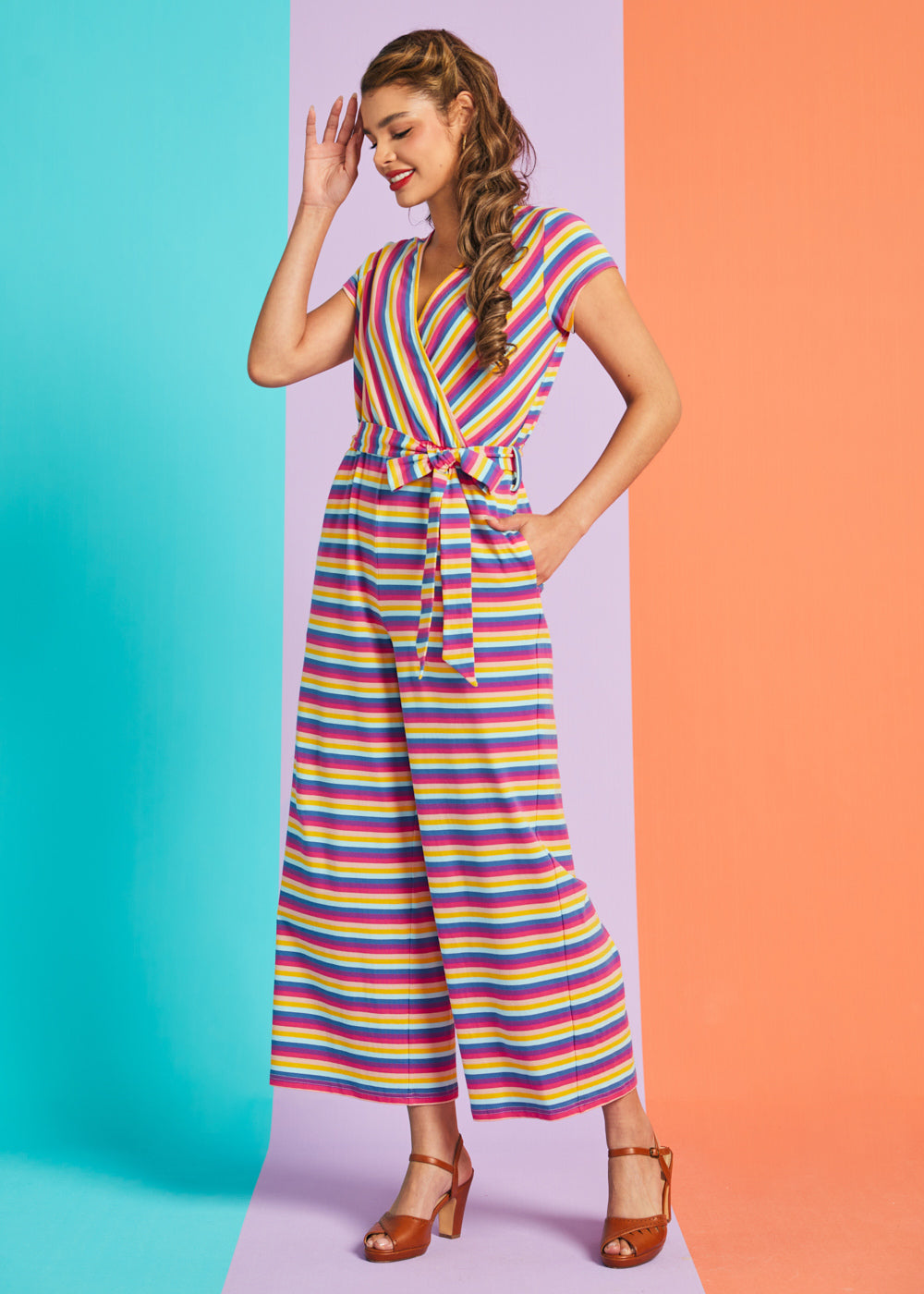 Woman wearing a colorful striped jumpsuit on a two-tone blue and orange background