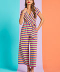Model wearing retro-inspired rainbow stripe jumpsuit with tie waist and wide legs