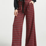 Woman wearing red tartan plaid wide leg pants with black sash belt and black top against a white studio background