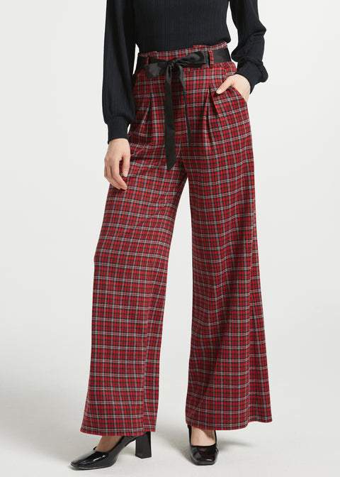 Woman wearing red tartan plaid wide leg pants with black sash belt and black top against a white studio background