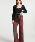 Full-length view woman wearing red tartan plaid wide leg pants with removable black bow belt and black heels against a white background