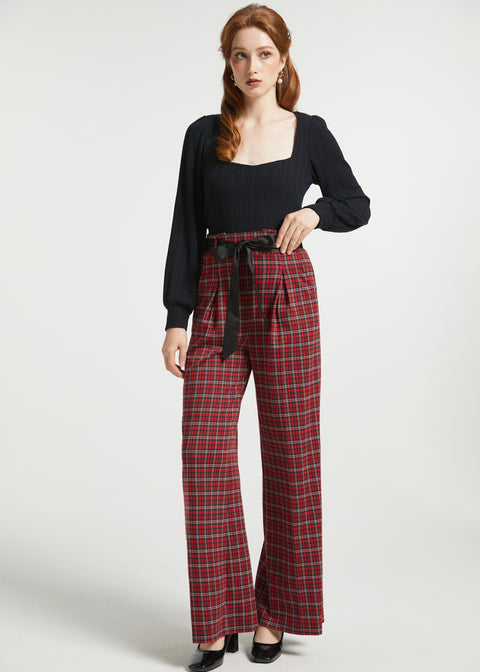 Full-length view woman wearing red tartan plaid wide leg pants with removable black bow belt and black heels against a white background