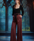Woman wearing high-waisted red tartan plaid wide leg pants with black bow belt and black square-neck top in a gothic window setting