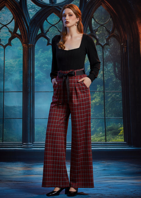 Woman wearing high-waisted red tartan plaid wide leg pants with black bow belt and black square-neck top in a gothic window setting