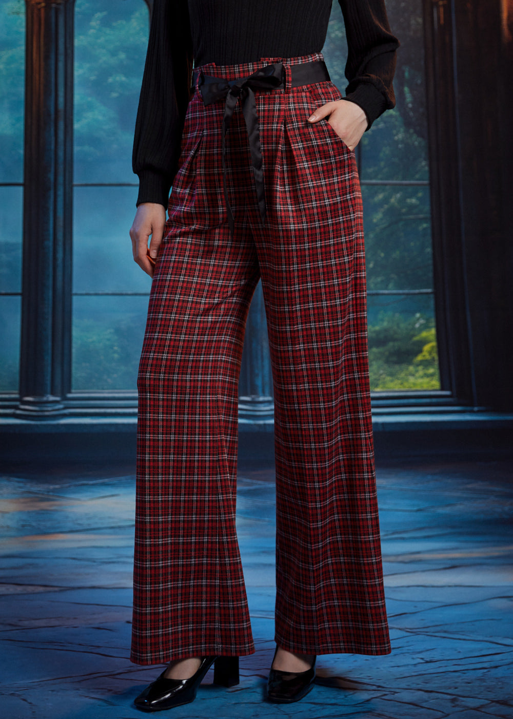 Woman wearing red tartan plaid wide leg pants with a black sash belt and side pockets, styled with a black long sleeve top