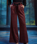 Woman wearing red tartan plaid wide leg pants with hands in the side pockets, showing the removable black bow sash belt