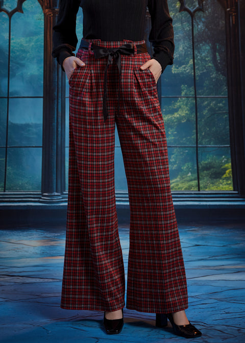 Woman wearing red tartan plaid wide leg pants with hands in the side pockets, showing the removable black bow sash belt