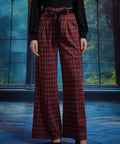 Front view of woman wearing red tartan plaid wide leg pants with black sash belt, showing the pleated waist and wide-leg fit