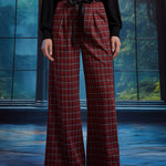 Front view of woman wearing red tartan plaid wide leg pants with black sash belt, showing the pleated waist and wide-leg fit