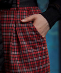 Close-up of red tartan plaid knit pants showing the front pleats, side pocket, belt loop, and removable black sash belt