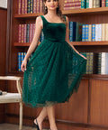 Woman wearing emerald green velvet tulle midi dress posed in front of bookshelves
