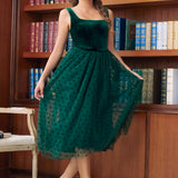 Woman wearing emerald green velvet tulle midi dress posed in front of bookshelves