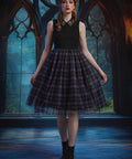 A young woman stands in a gothic-style room with large arched windows, wearing a sleeveless dress with black top and a full black-and-purple plaid skirt with a patterned collar and black boots.