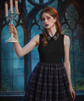 A woman with red hair stands in a gothic-style room with large arched windows, holding a white candelabra. She is wearing a sleeveless dress with black bodice, a decorative collar and a dark plaid skirt.