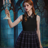 A woman with red hair stands in a gothic-style room with large arched windows, holding a white candelabra. She is wearing a sleeveless dress with black bodice, a decorative collar and a dark plaid skirt.
