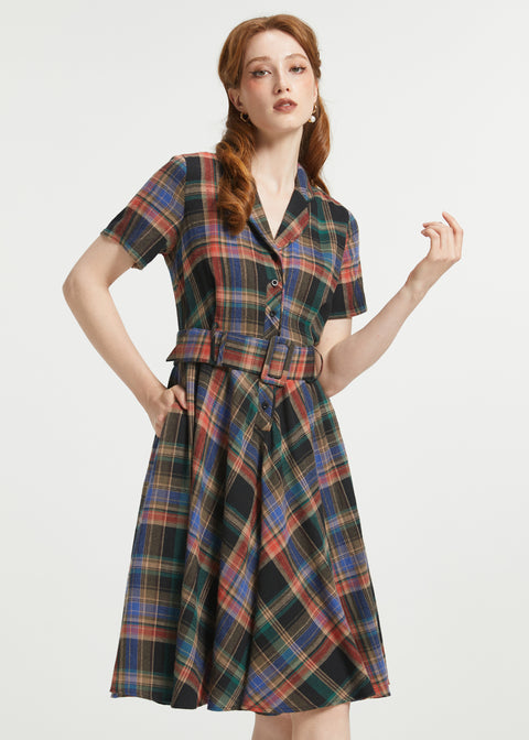 A woman modeling a short-sleeve plaid dress with a collared neckline, button front, and matching tie belt, shown against a plain light gray studio background.