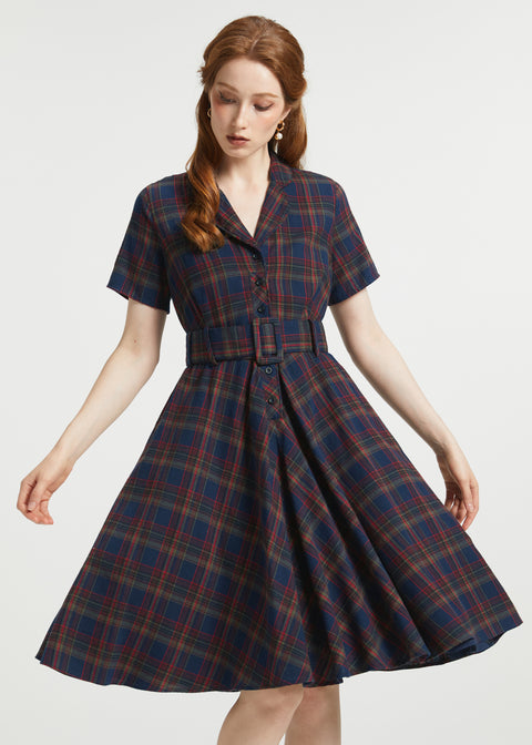 A woman modeling a short-sleeve plaid dress with a button front and matching belt, shown against a plain light gray studio background.
