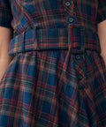 Close-up of a plaid dress with a matching belt, featuring blue, red, and green tartan pattern with dark buttons.