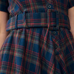 Close-up of a plaid dress with a matching belt, featuring blue, red, and green tartan pattern with dark buttons.