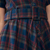 Close-up of a plaid dress with a matching belt, featuring blue, red, and green tartan pattern with dark buttons.