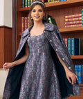A woman models a vintage-style dress with a matching patterned cape and headband in front of a wooden bookshelf.