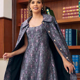 A woman models a vintage-style dress with a matching patterned cape and headband in front of a wooden bookshelf.