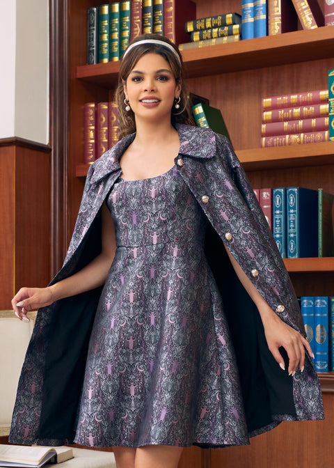 A woman models a vintage-style dress with a matching patterned cape and headband in front of a wooden bookshelf.