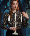 Woman styling gothic skull and floral button-up blouse with candelabra