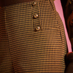 Close-up of golden brown and black houndstooth pants showing the high waist and decorative gold-tone buttons