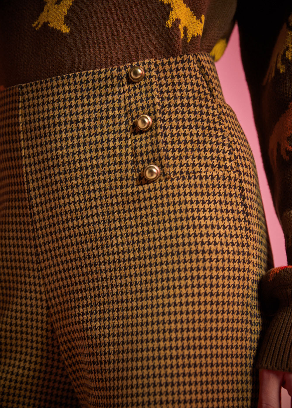 Close-up of golden brown and black houndstooth pants showing the high waist and decorative gold-tone buttons