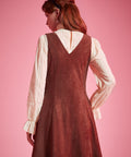 Back view of woman wearing sleeveless V-back A-line jumper dress in rust brown