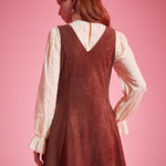 Back view of woman wearing sleeveless V-back A-line jumper dress in rust brown