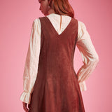 Back view of woman wearing sleeveless V-back A-line jumper dress in rust brown
