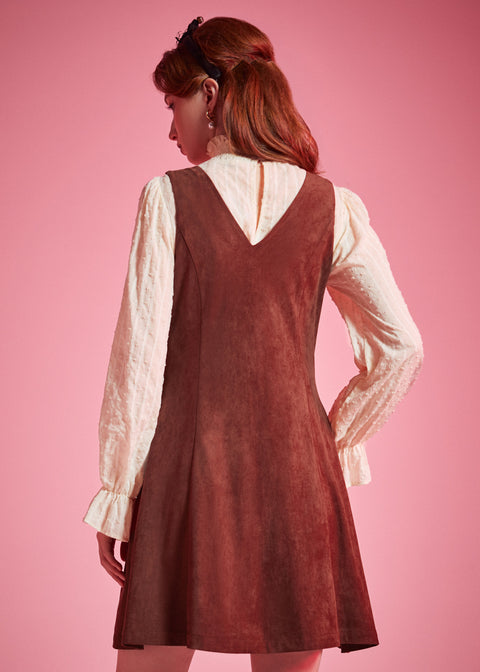 Back view of woman wearing sleeveless V-back A-line jumper dress in rust brown
