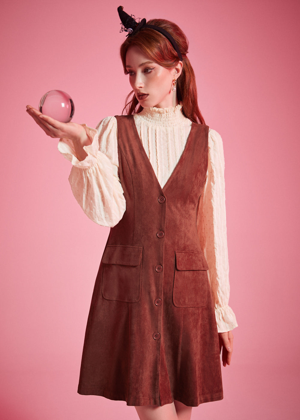 Woman wearing rust brown A-line button front jumper dress layered over cream blouse